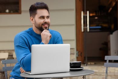 Photo of Handsome young man with laptop at table in outdoor cafe. Space for text
