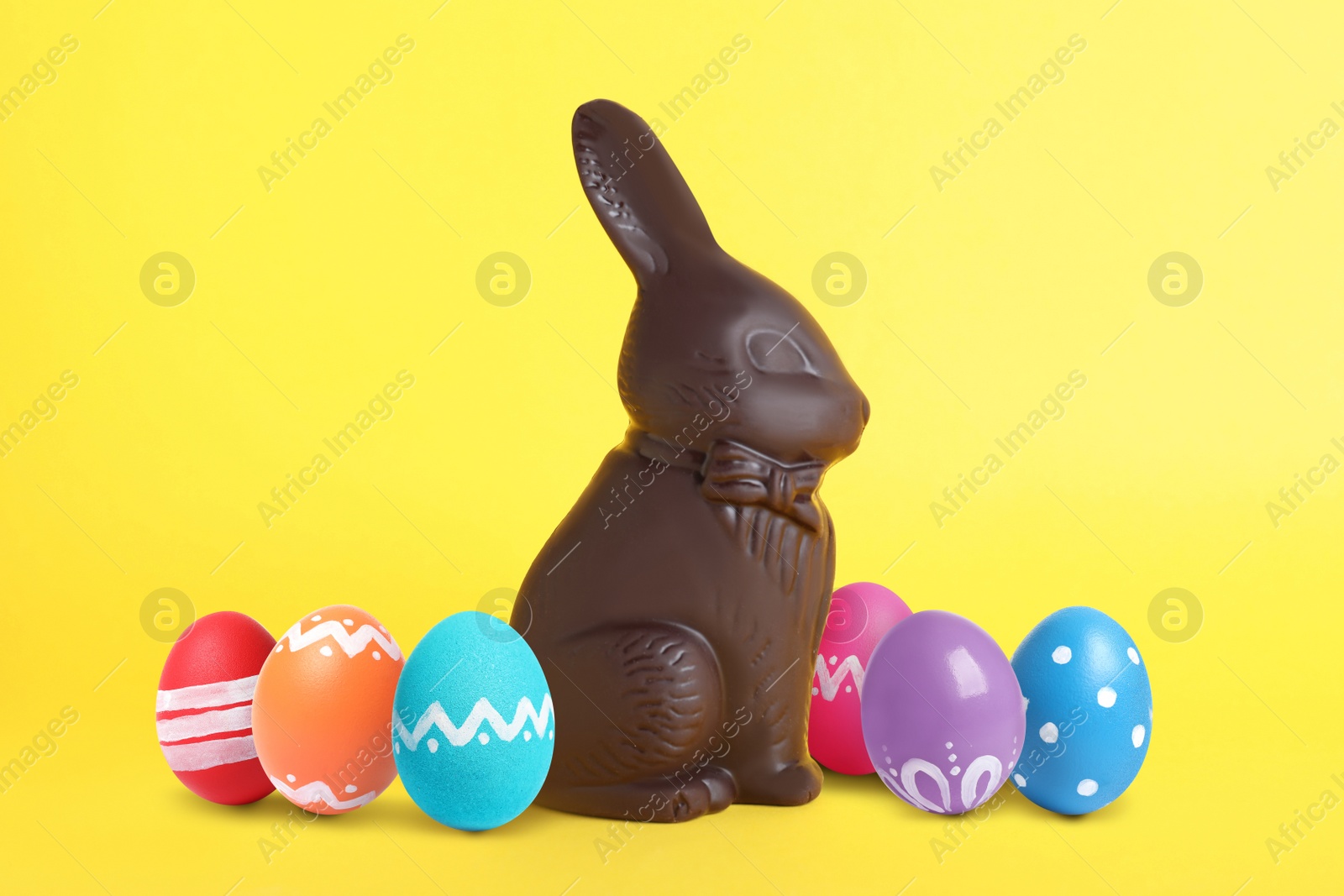 Image of Chocolate bunny and painted Easter eggs on yellow background