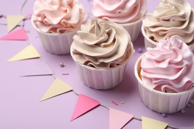 Photo of Delicious birthday cupcakes, sprinkles and bunting flags on violet background, closeup