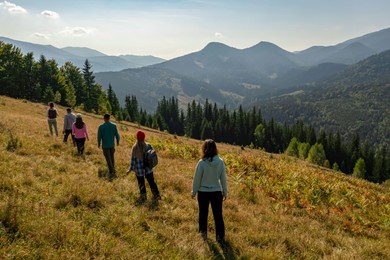 Image of Group of tourists walking on hill in mountains, back view