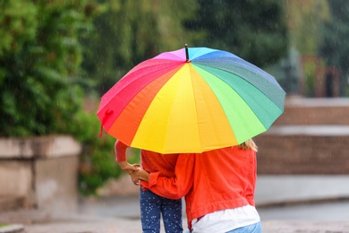 Photo of Mother and daughter with bright umbrella under rain outdoors