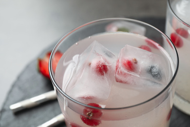 Glass of refreshing drink with ice cubes and berries on table, closeup