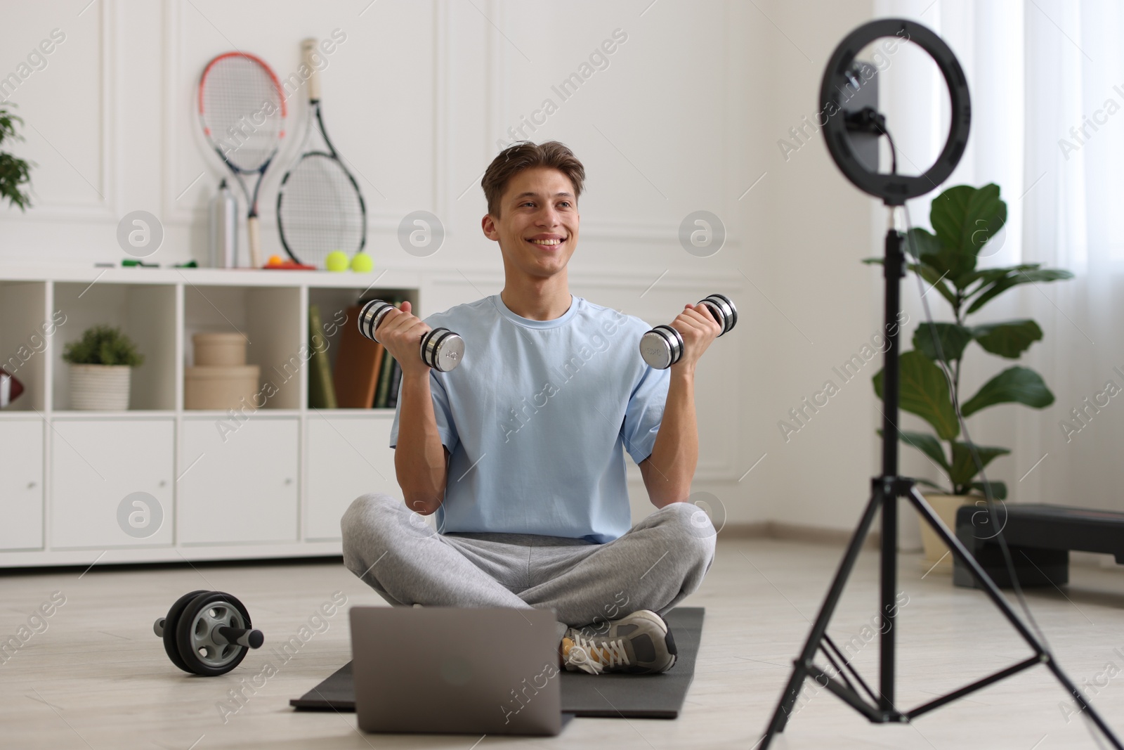 Photo of Smiling sports blogger working out with dumbbells while streaming online fitness lesson at home