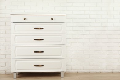 Photo of Modern chest of drawers near white brick wall. Space for text