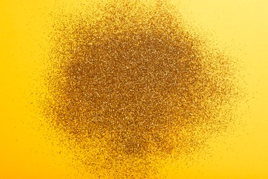 Photo of Shiny golden glitter on yellow background, top view