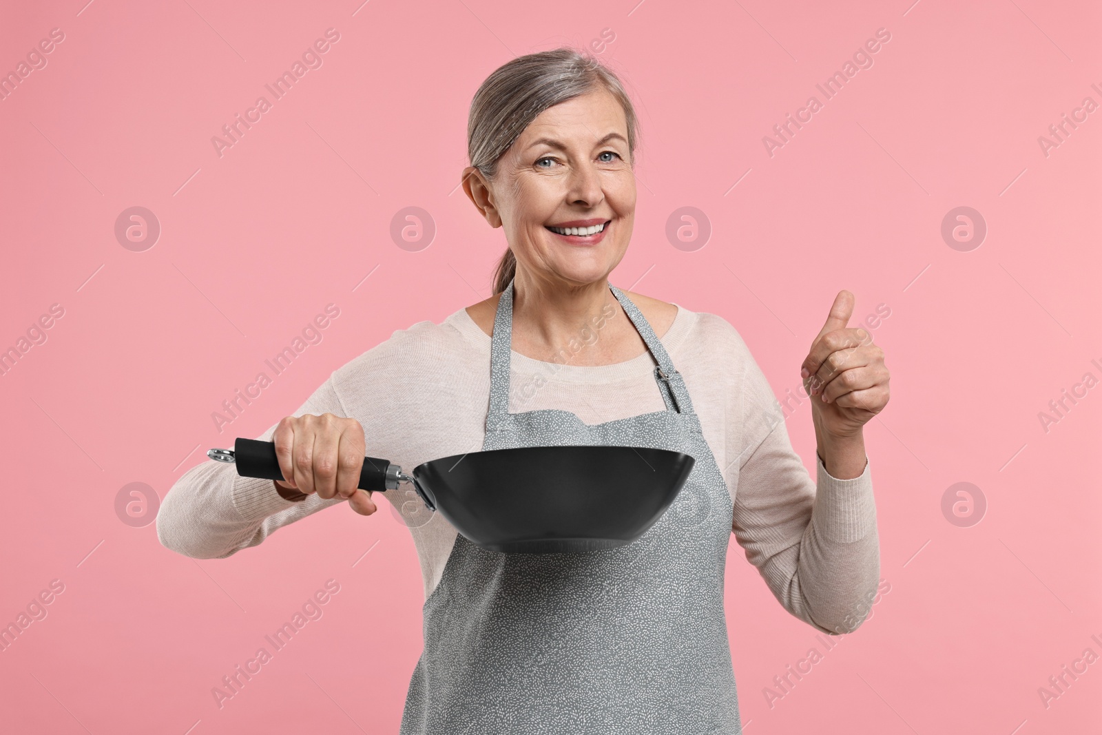 Photo of Happy housewife with frying pan showing thumbs up on pink background