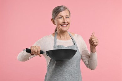 Photo of Happy housewife with frying pan showing thumbs up on pink background