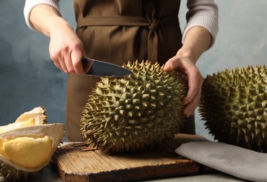 Photo of Woman cutting durian at table against blue background, closeup