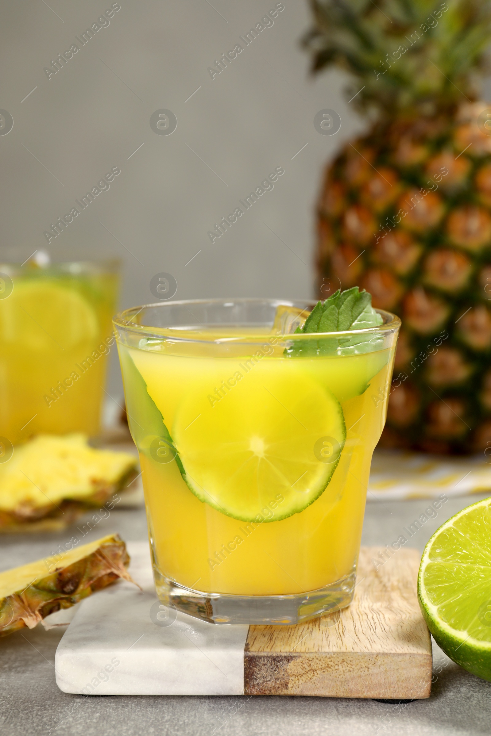 Photo of Glasses of tasty pineapple cocktail with mint and lime on light grey table