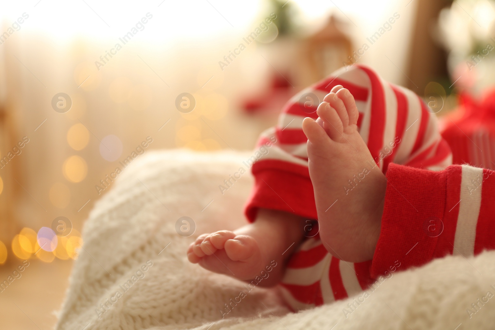 Photo of Cute little baby on knitted blanket in room against Christmas lights, closeup. Space for text