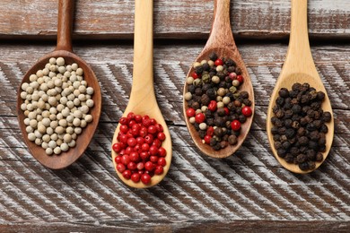 Photo of Aromatic spice. Different peppers in spoons on wooden table, flat lay