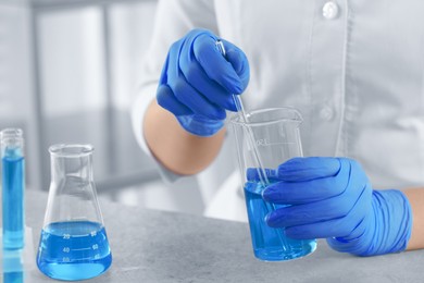 Photo of Scientist taking sample of light blue liquid in laboratory, closeup