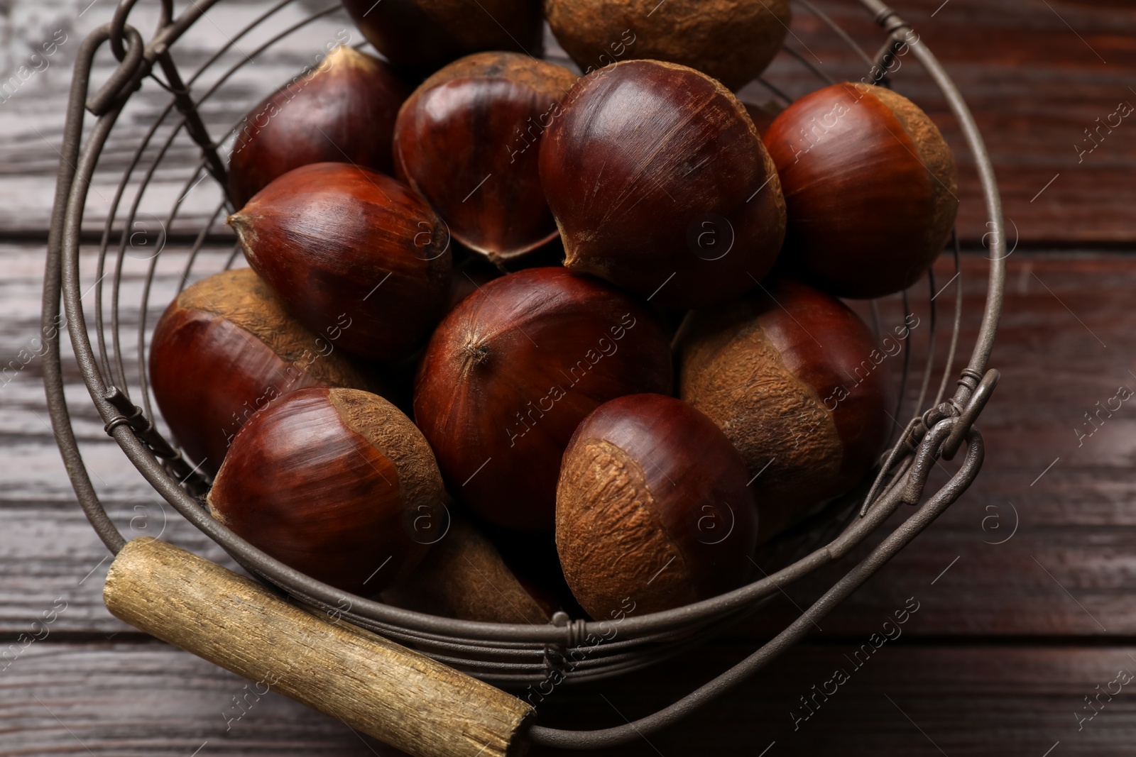 Photo of Sweet fresh edible chestnuts in metal basket on wooden table, closeup