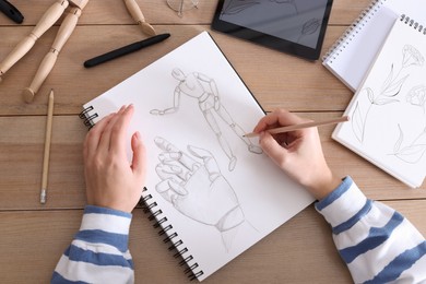 Photo of Woman drawing in sketchbook with pencil at wooden table, top view
