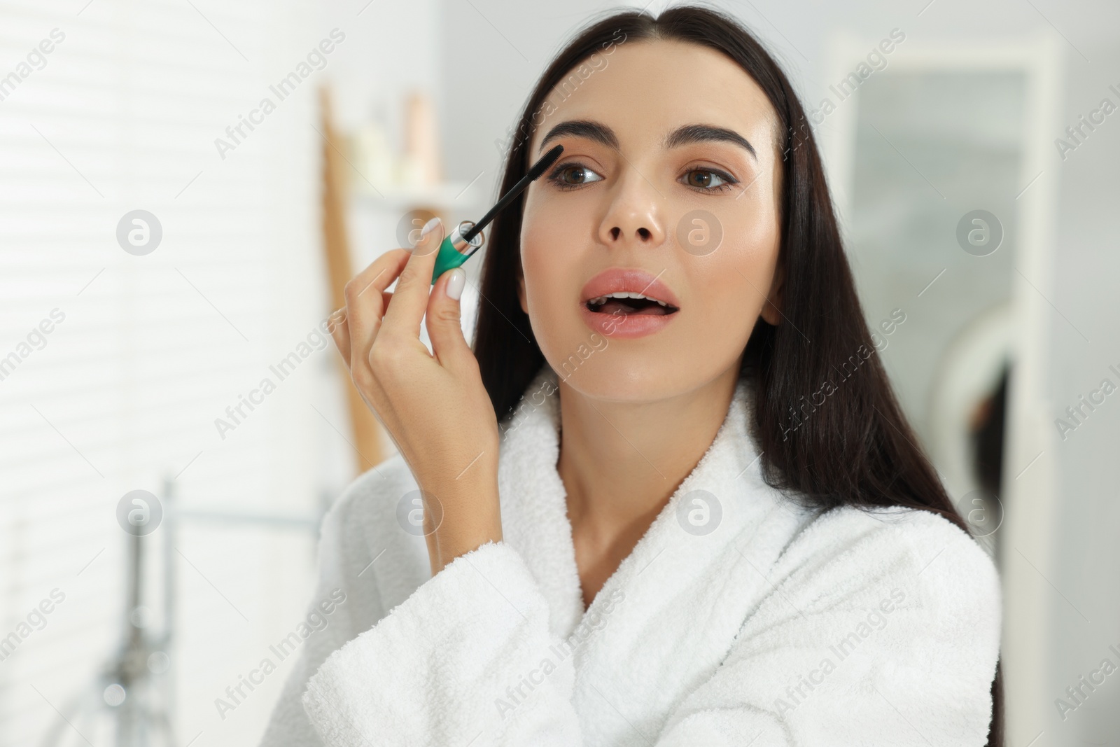 Photo of Beautiful young woman applying mascara in bathroom