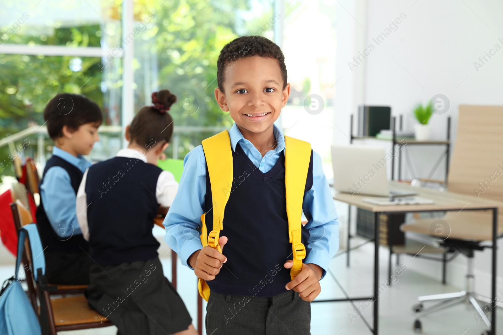 Photo of African-American boy wearing school uniform with backpack in classroom