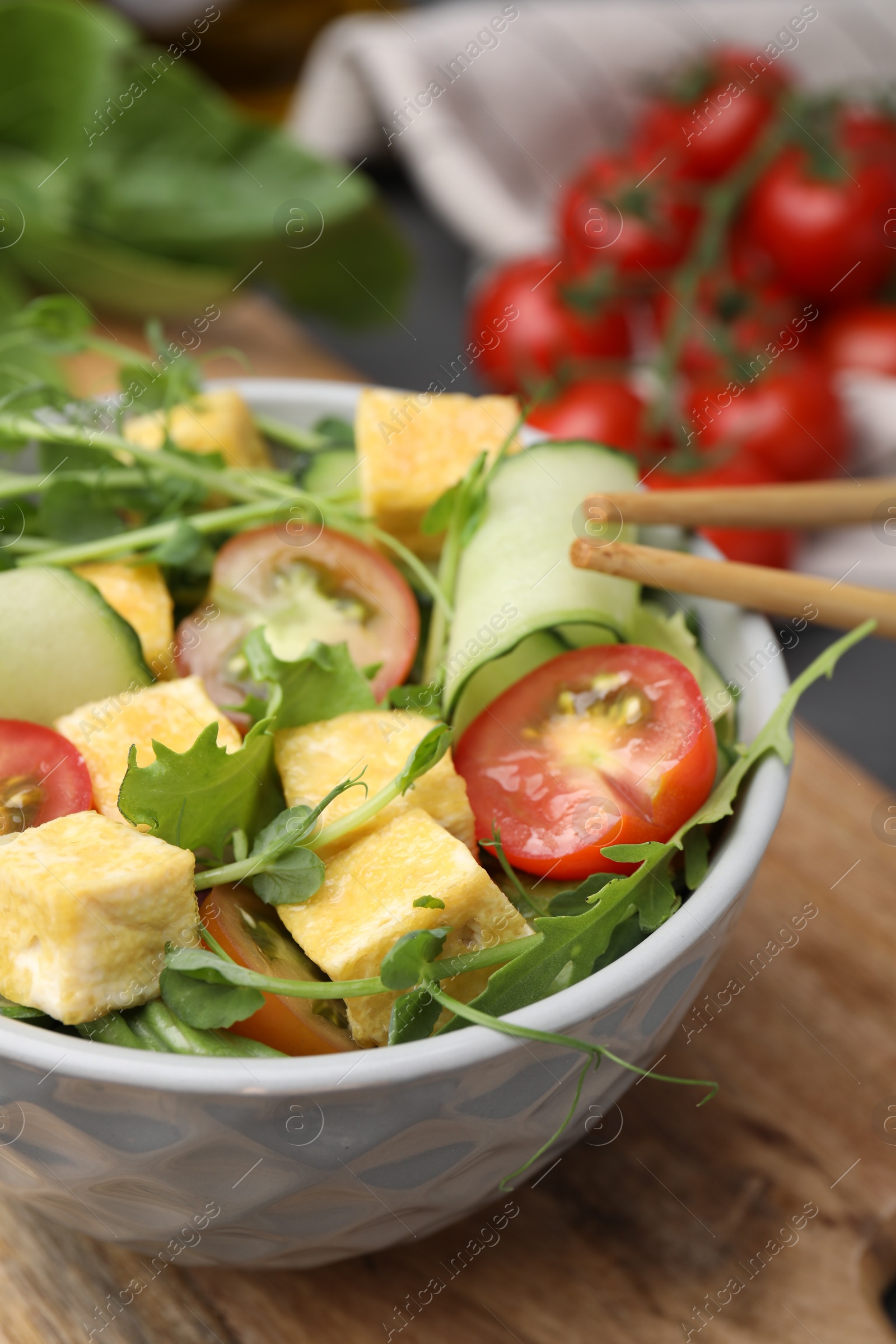 Photo of Bowl of tasty salad with tofu and vegetables on wooden board, closeup