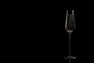 Photo of Glass of champagne on black background, space for text