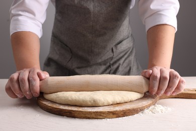 Man rolling dough with wooden pin at white table near grey wall, closeup