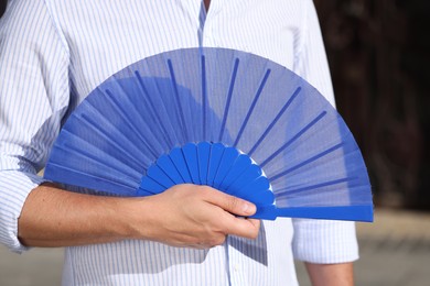 Photo of Man with blue hand fan outdoors, closeup