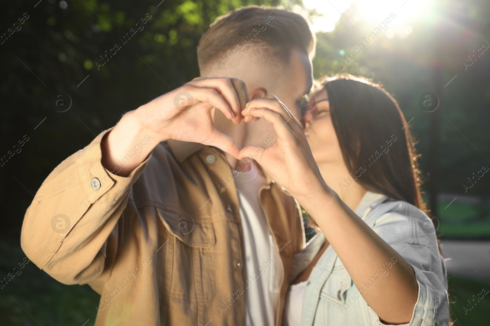 Photo of Affectionate young couple kissing and making heart with hands in park