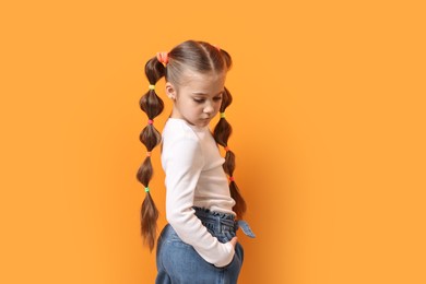 Photo of Cute little girl with beautiful hairstyle on orange background. Space for text