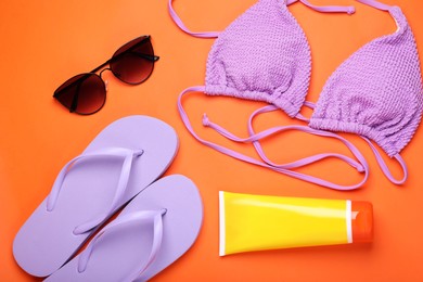 Photo of Tube of sunscreen, sunglasses, flip flops and swimsuit top on orange background, flat lay. Sun protection care