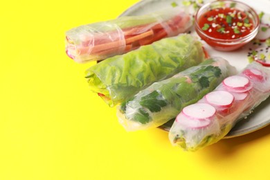Photo of Delicious spring rolls served with sauce on yellow background, closeup. Space for text