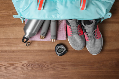 Photo of Open sports bag with gym stuff on wooden background, flat lay