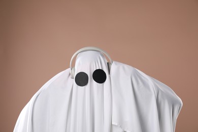 Person in ghost costume wearing headphones on dark beige background