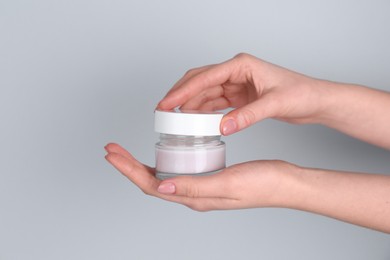 Woman holding jar of cream on grey background, closeup