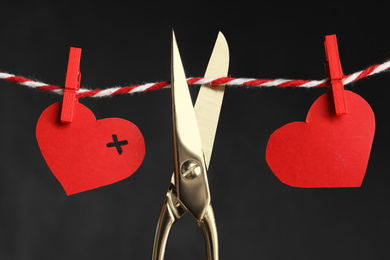 Photo of Red paper hearts on rope and scissors against black background. Composition symbolizing problems in relationship