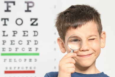 Photo of Cute little boy with magnifier visiting ophthalmologist