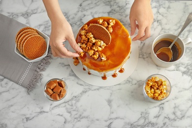 Young woman decorating delicious homemade cake at table, top view