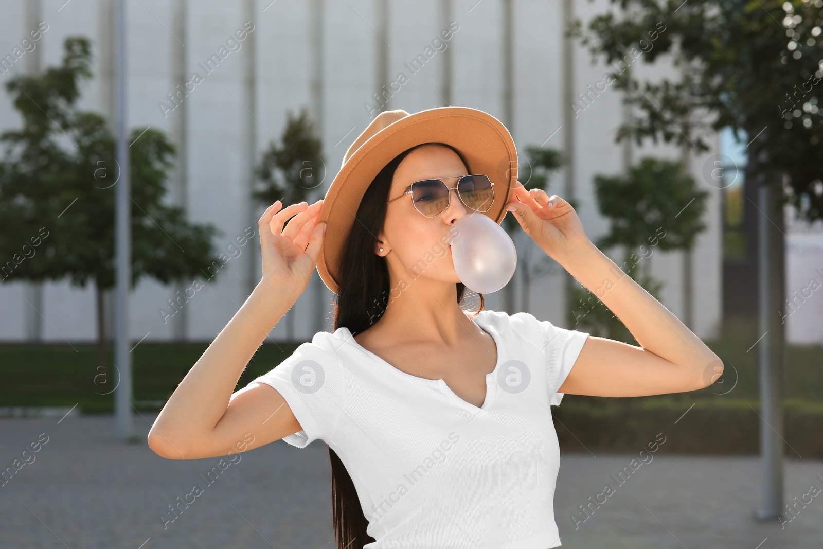 Photo of Beautiful woman in stylish sunglasses blowing gum outdoors on sunny day