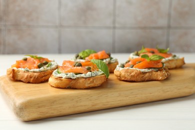 Photo of Tasty canapes with salmon, capers and sauce on white wooden table, closeup