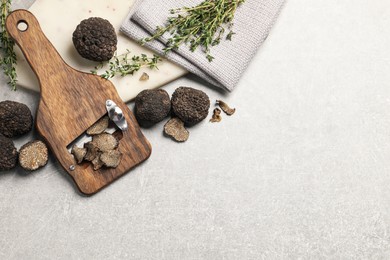 Fresh black truffles, slicer and thyme on grey table, flat lay. Space for text