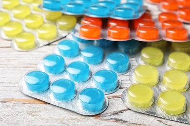 Photo of Blisters with color cough drops on wooden table, closeup