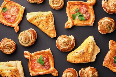 Various delicious puff pastry with tasty filling on black background, flat lay