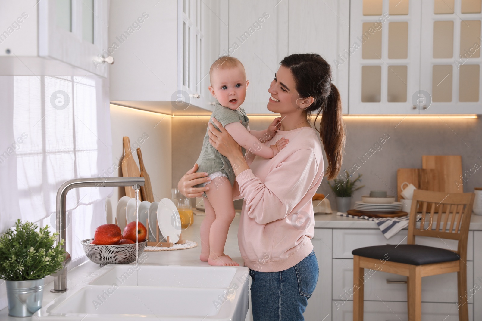 Photo of Happy young woman and her cute little baby spending time together in kitchen