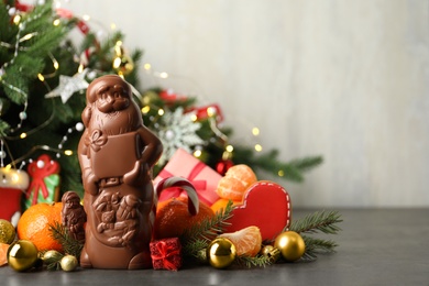 Composition with chocolate Santa Claus candies on grey table near Christmas tree, space for text