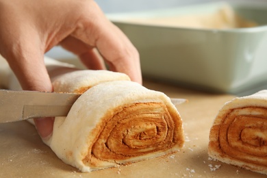 Woman cutting dough for cinnamon rolls on parchment at table, closeup