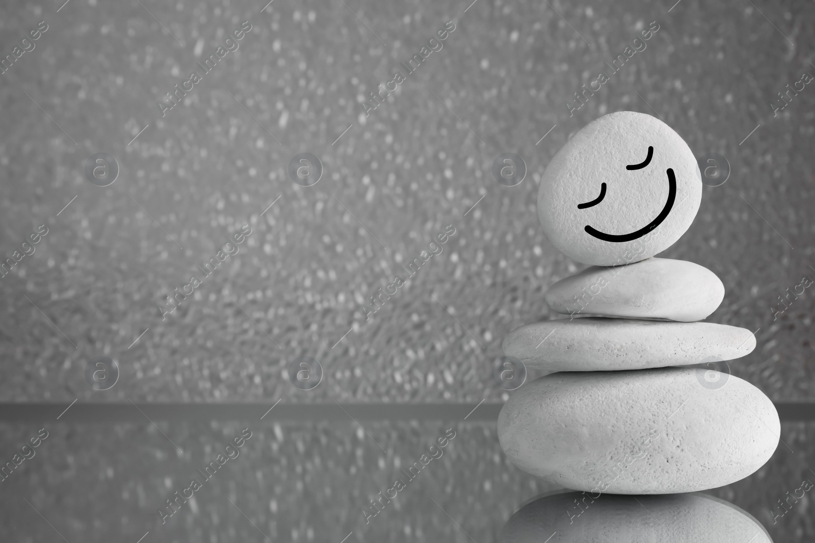 Photo of Stack of stones with drawn happy face on grey background, space for text. Zen concept