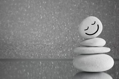 Photo of Stack of stones with drawn happy face on grey background, space for text. Zen concept