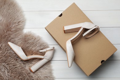 Photo of Pair of stylish shoes, cardboard box and faux fur on white wooden background, flat lay