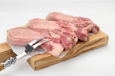 Photo of Raw beef tongue pieces and carving fork on white wooden table, closeup
