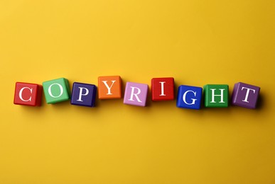 Photo of Plagiarism concept. Word Copyright made of color cubes on yellow background, top view
