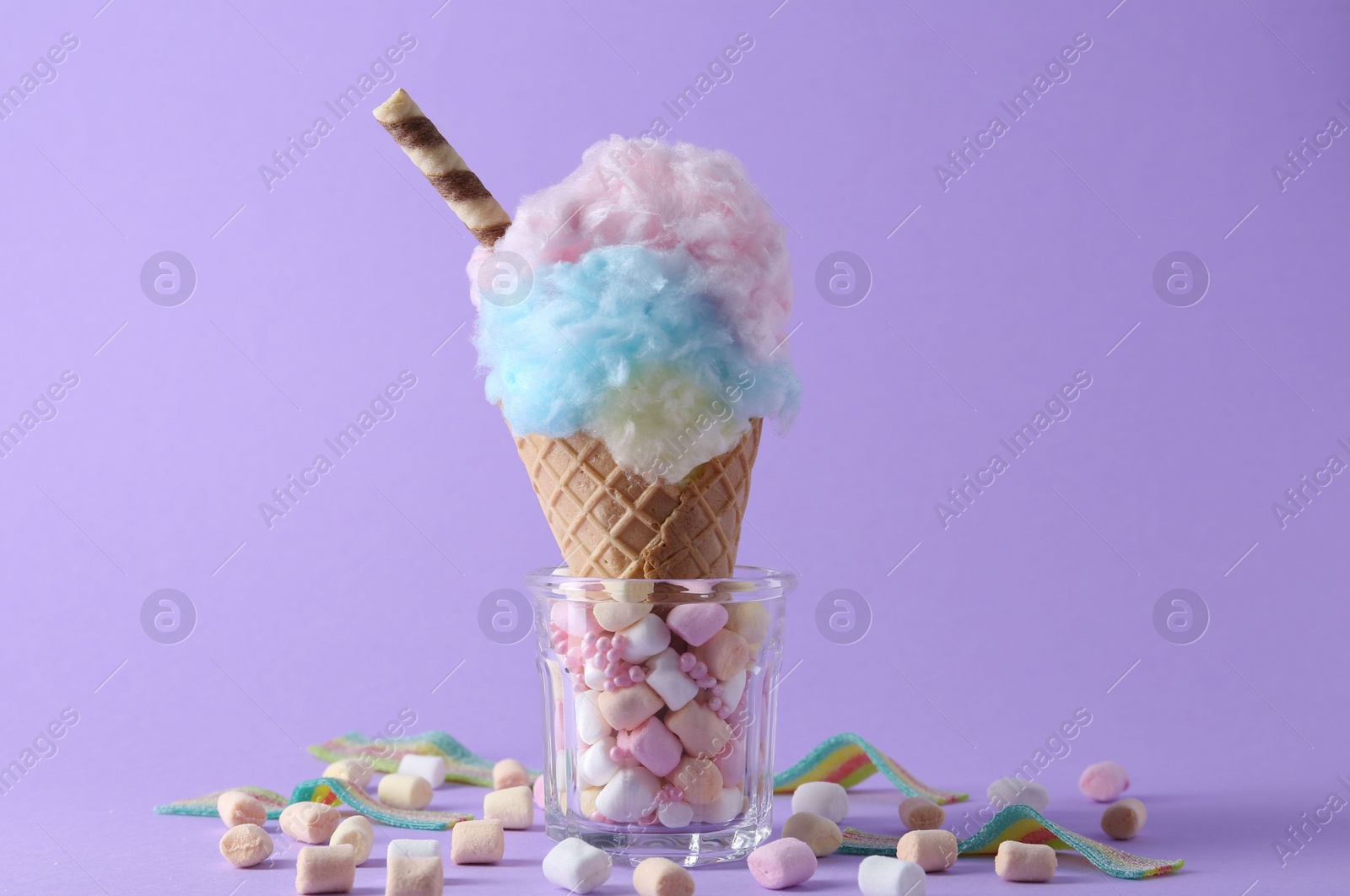 Photo of Sweet cotton candy in waffle cone and marshmallows on purple background, closeup