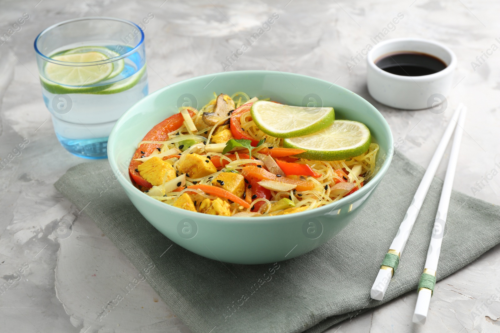 Photo of Stir-fry. Delicious cooked noodles with chicken and vegetables in bowl served on gray textured table