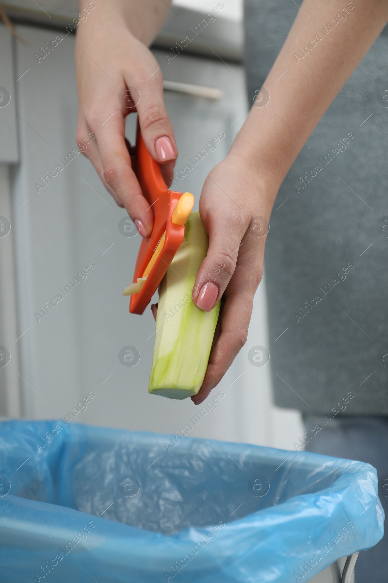 Photo of Woman peeling fresh zucchini above garbage bin indoors, closeup